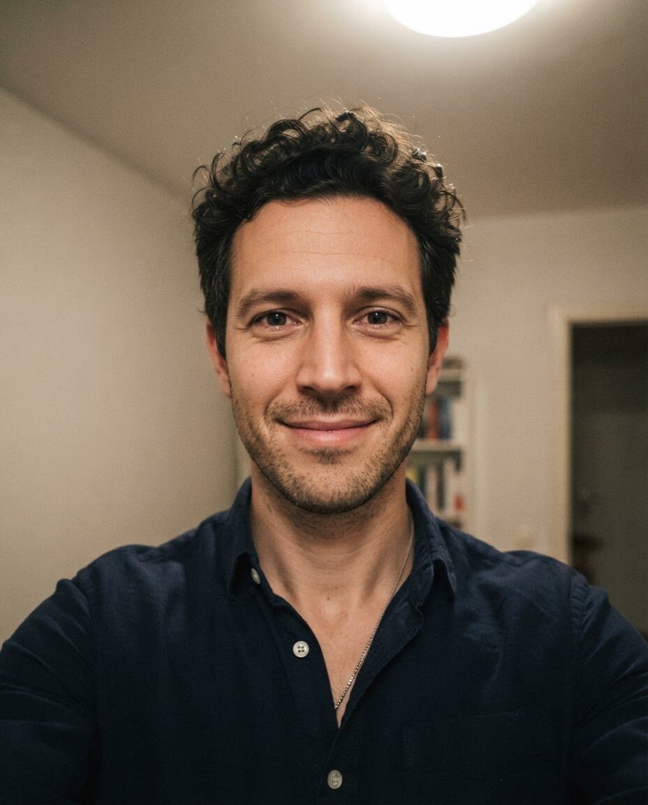 Sam's portrait: a live selfie of a man with short curly hair, smiling into the camera